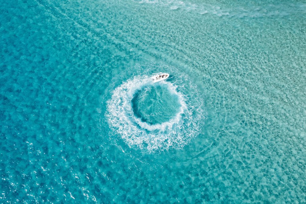 Aerial shot of a boat creating circular waves in the turquoise waters of Sardinia.