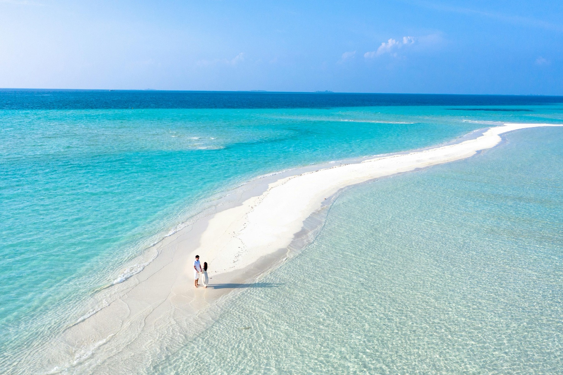 Couple walking along an empty beach on a private island holiday at sunset