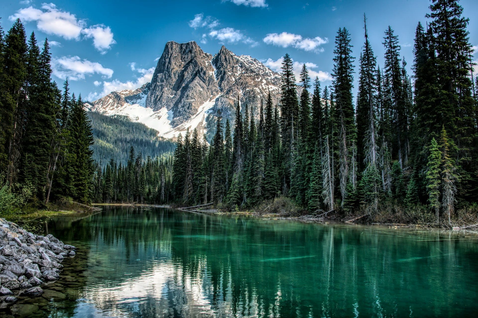 A snow-capped mountain reflected in an emerald forest lake in British Columbia