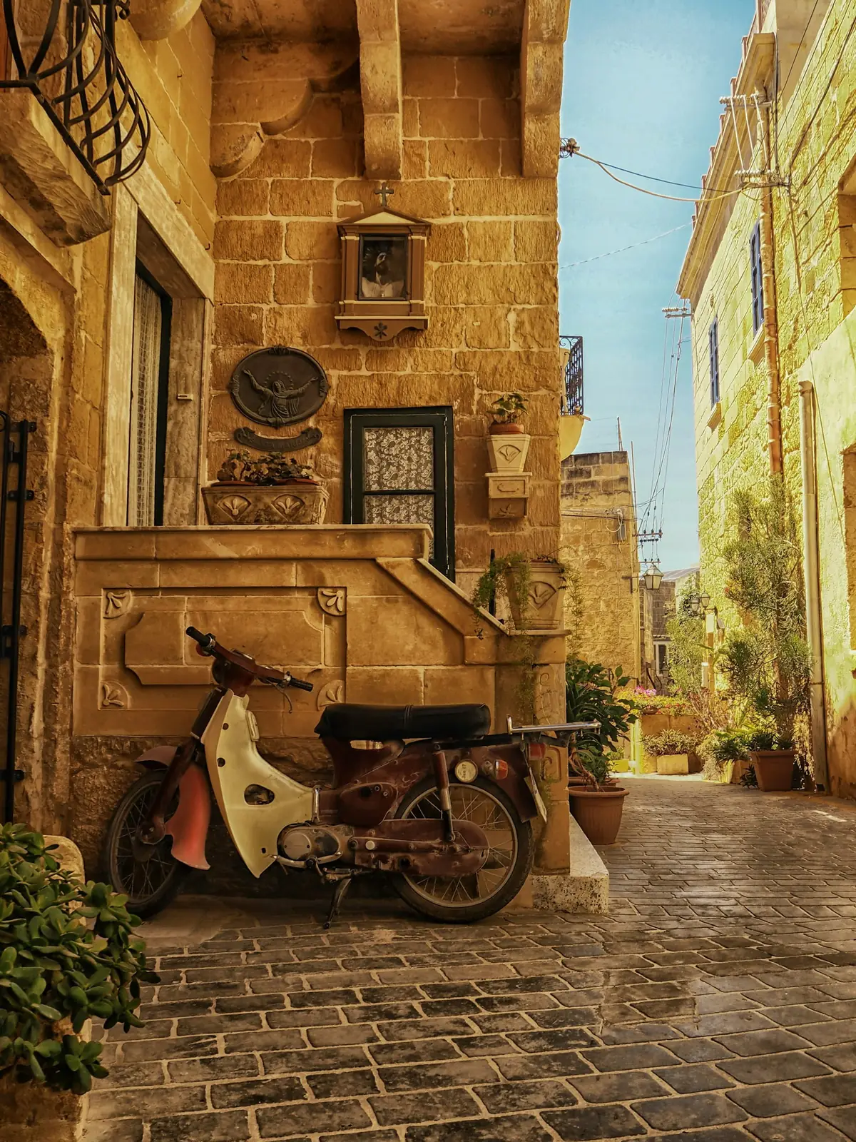 A vintage moped on a quiet cobbled village lane lined with honey-stone houses on Gozo, Malta