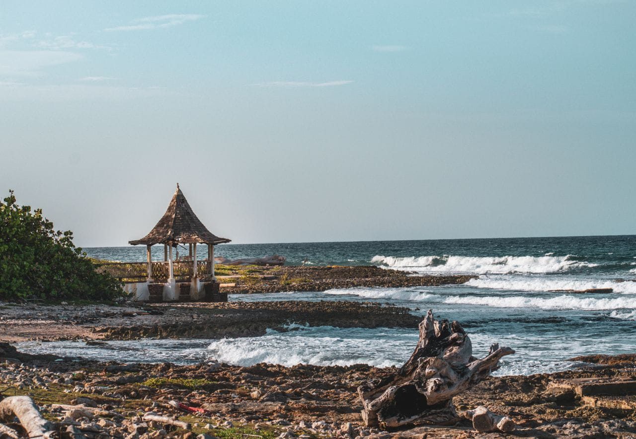 A thatched gazebo on a rugged rocky shore with breaking waves on Jamaica's south coast