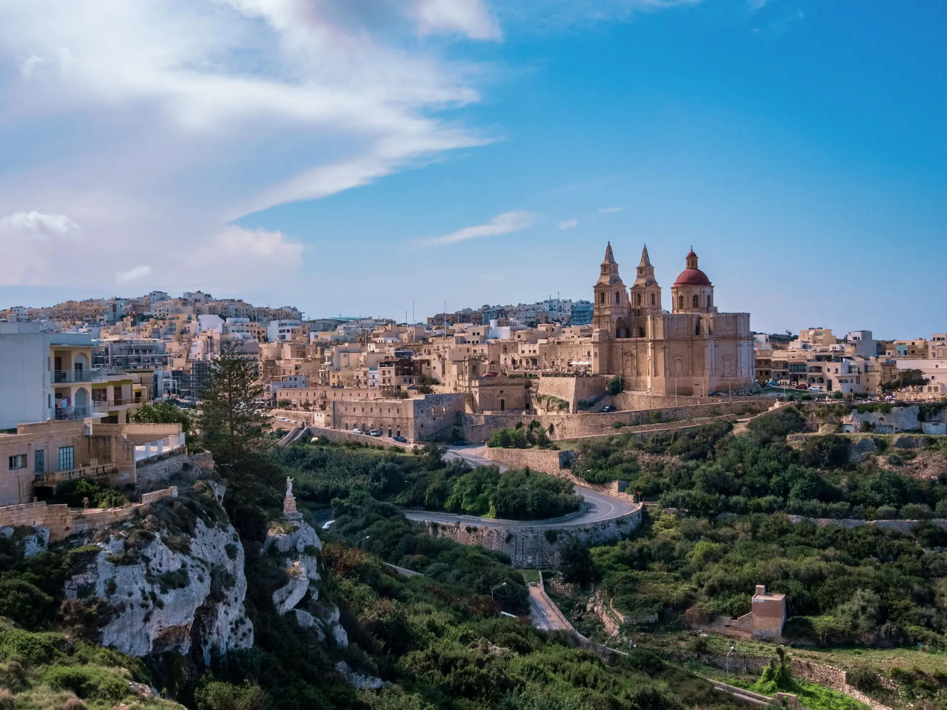 The honey-stone hilltop town of Mellieha crowned by its parish church, above green countryside in Malta