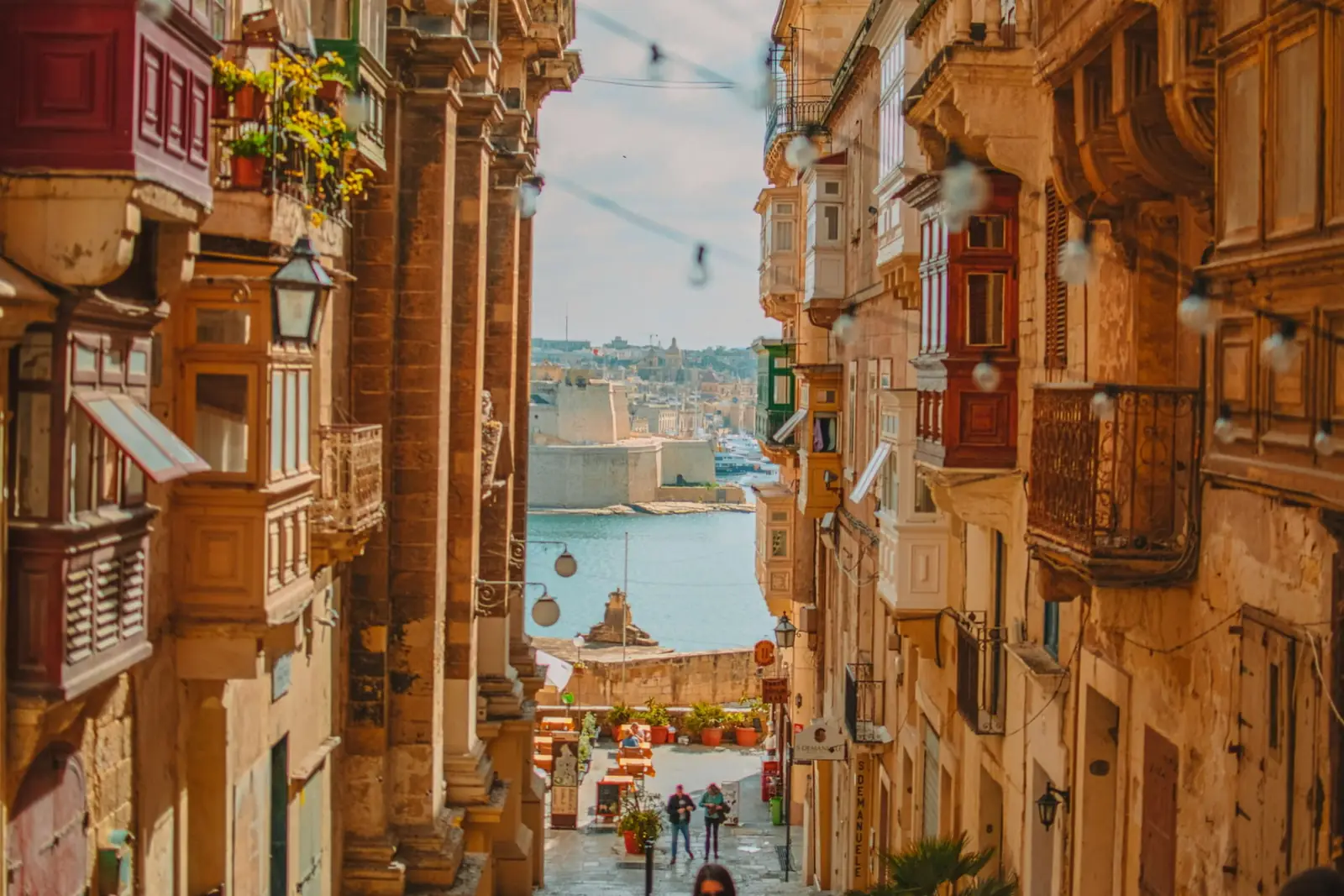 A stepped Valletta street framed by traditional Maltese balconies looking down to the Grand Harbour, Malta