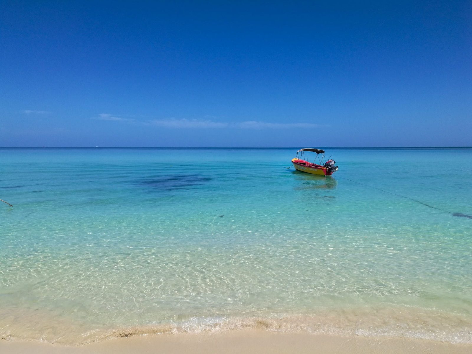A small boat on calm turquoise water off the white sand of Seven Mile Beach in Negril, western Jamaica