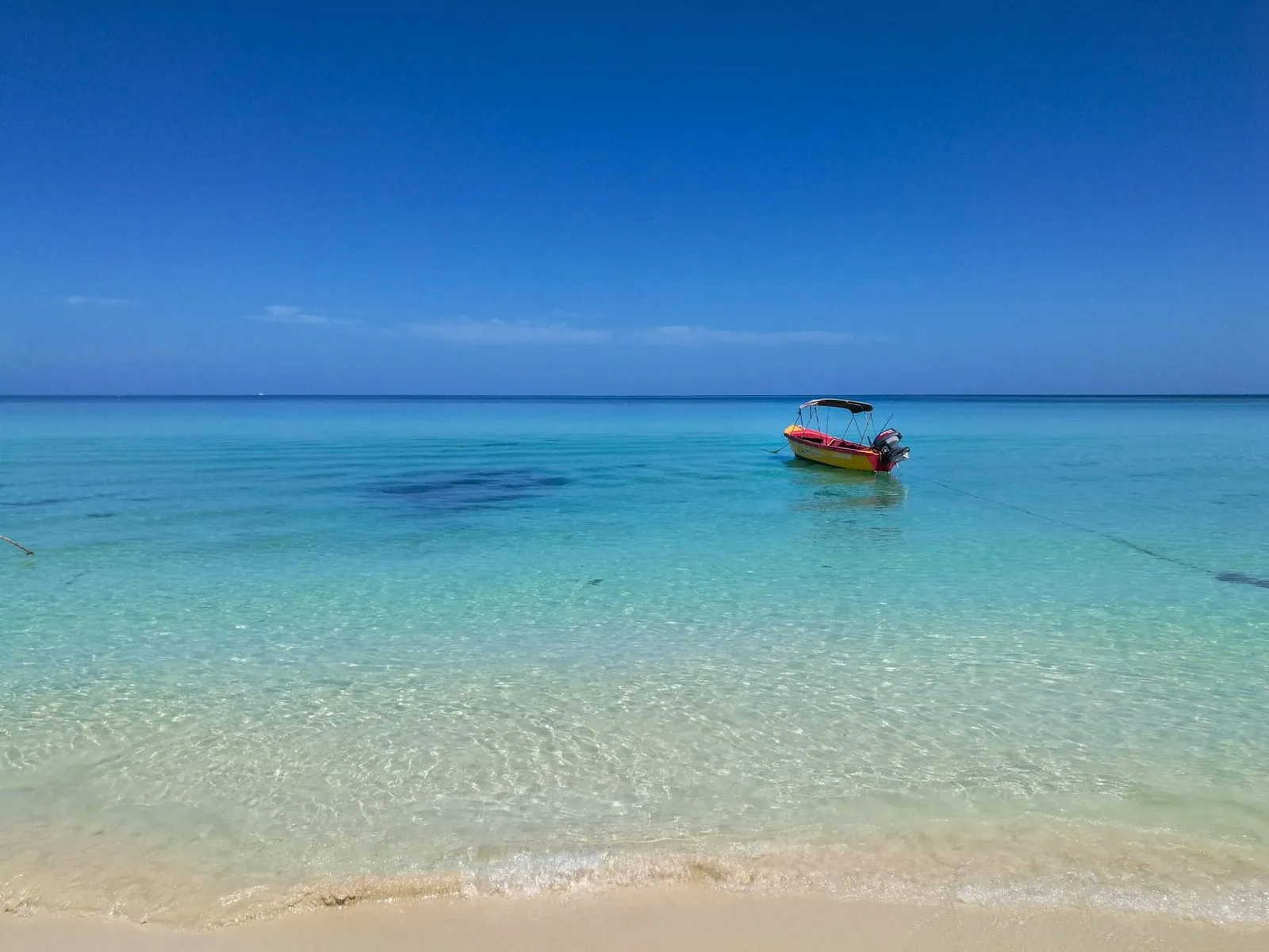 A small boat on calm turquoise water off the white sand of Seven Mile Beach in Negril, western Jamaica