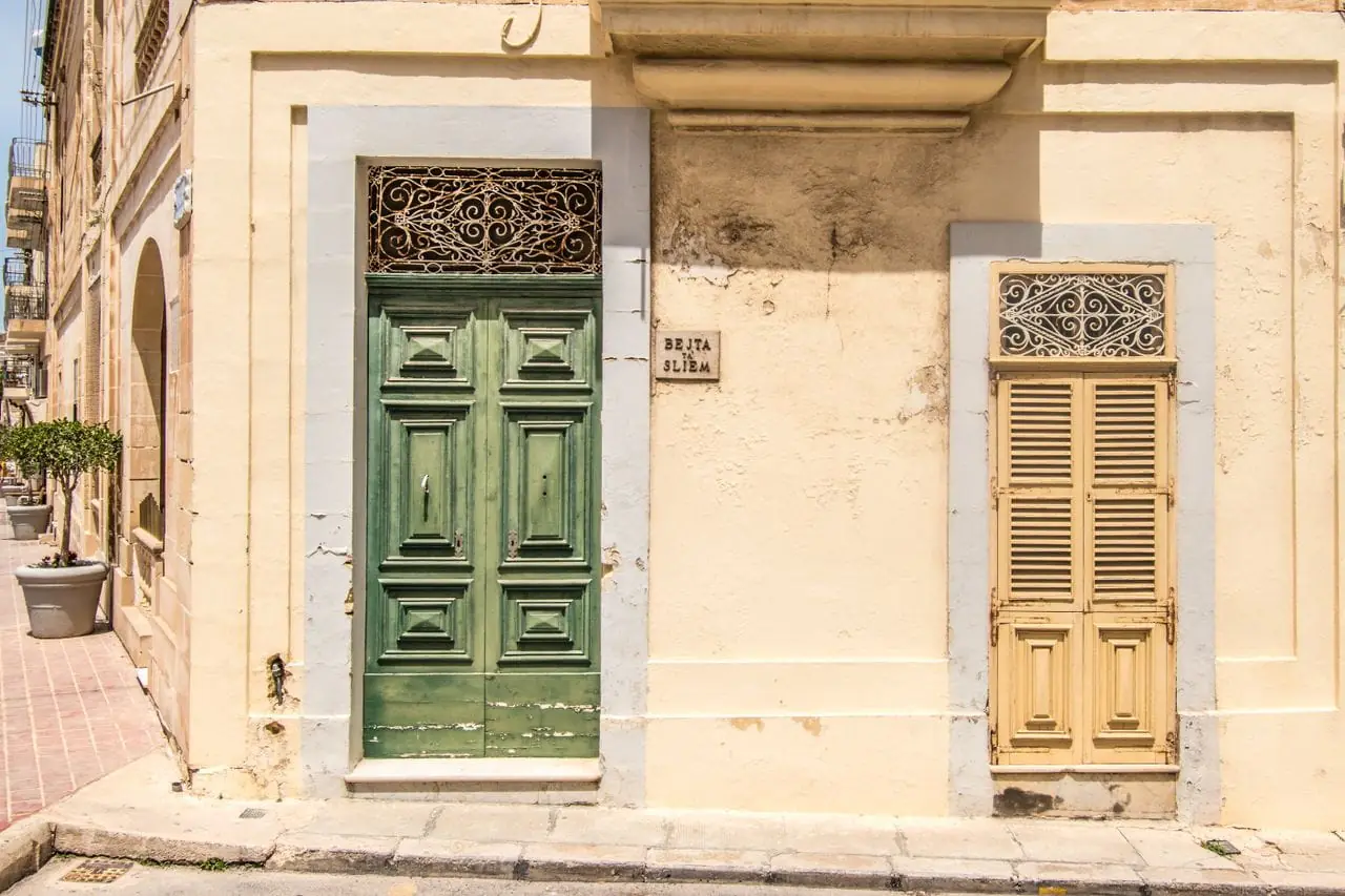 A traditional green door and shuttered window on a honey-stone townhouse in Sliema, Malta