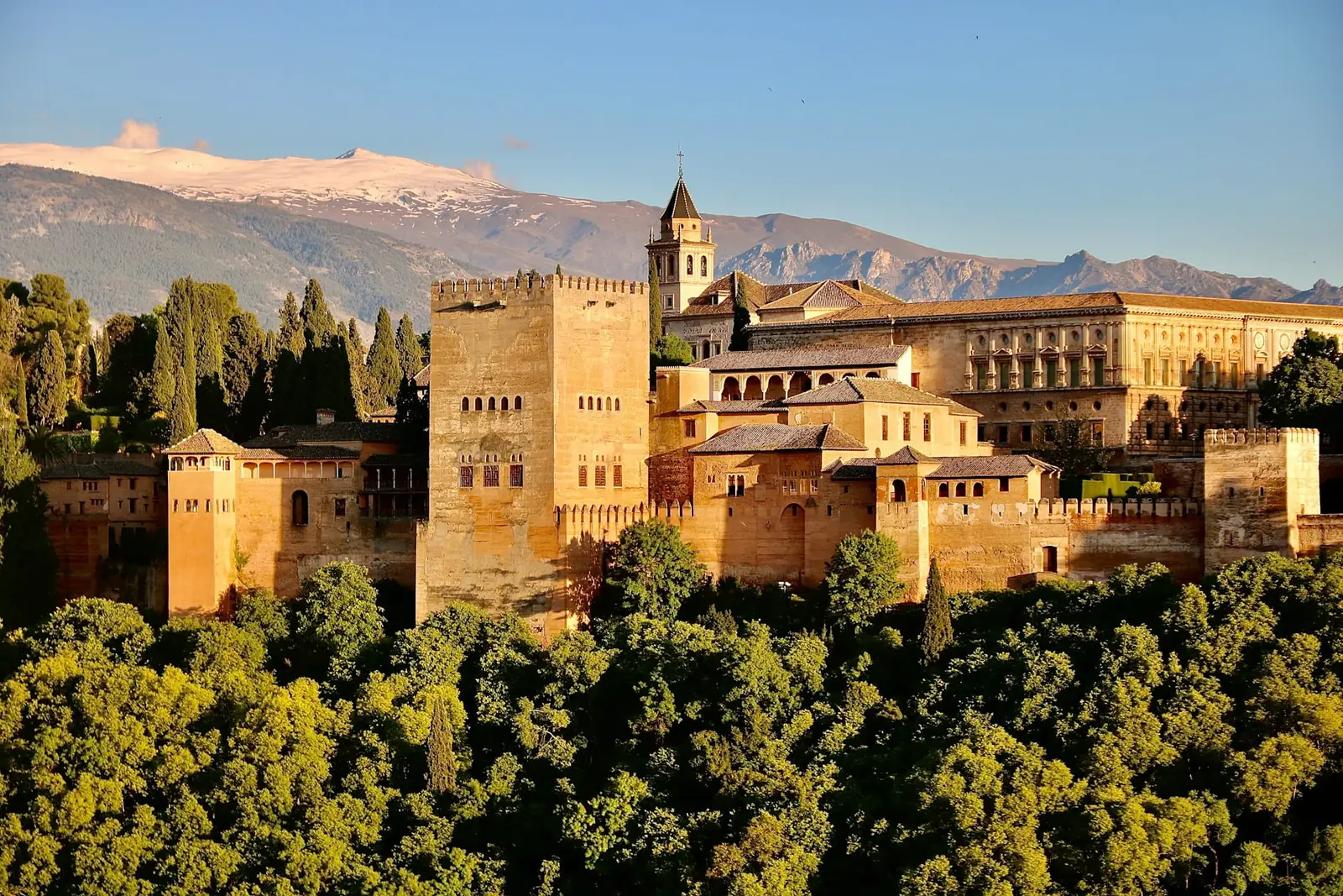 The Alhambra palace fortress above wooded hills with the snow-capped Sierra Nevada behind, Granada, Spain