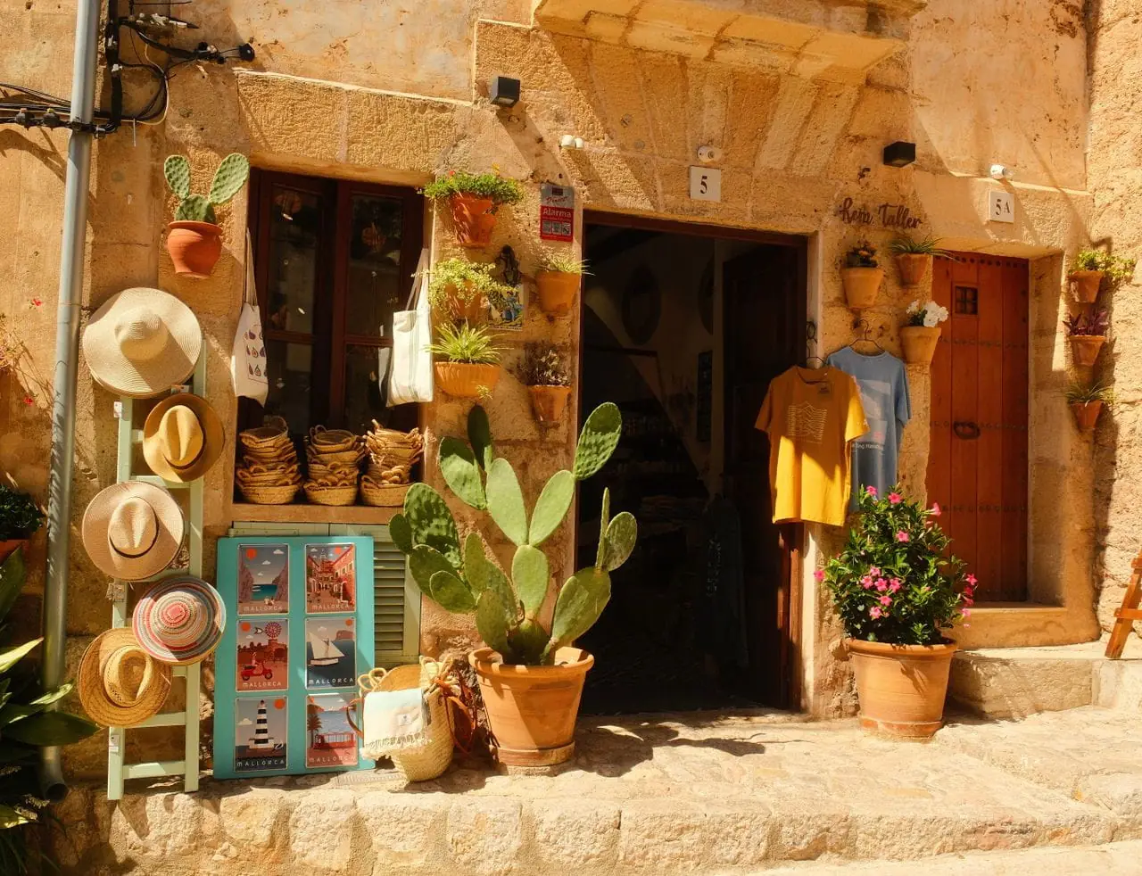 A sunlit village shopfront with straw hats and Mallorca postcards in a honey-stone Mallorcan town, Spain