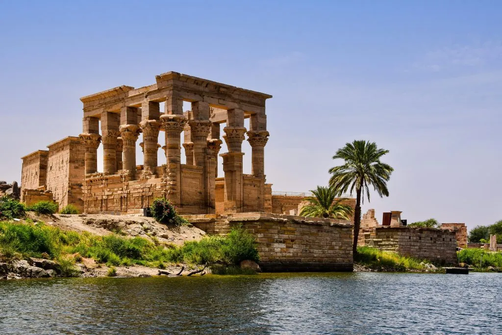 Ancient temple ruins near the Nile River with a palm tree and clear sky.