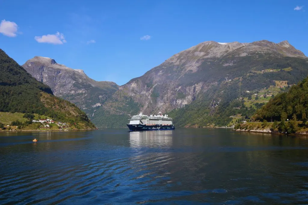 A majestic cruise ship in the scenic Geiranger Fjord, surrounded by mountains.