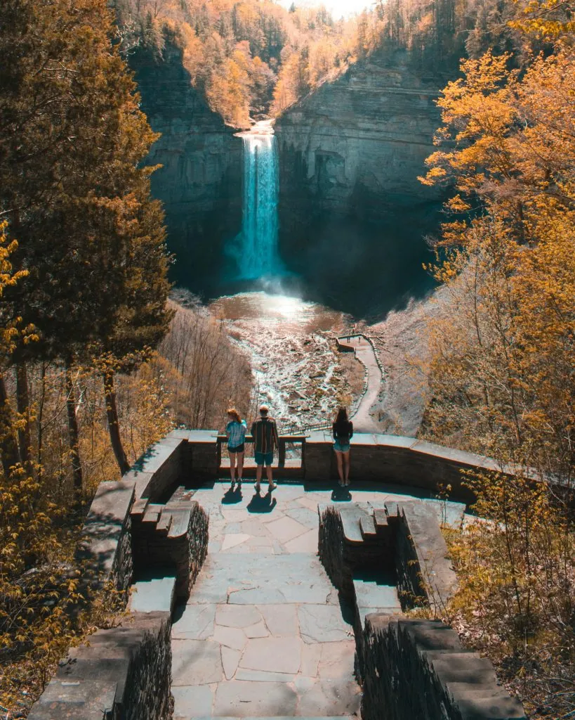 Tourists admire the stunning Taughannock Falls surrounded by vibrant autumn foliage in New York.