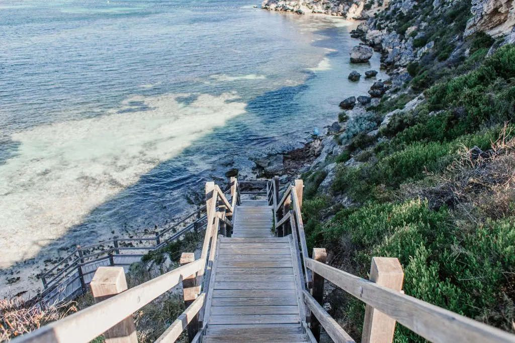 Wooden stairs descending to a tranquil beach with crystal clear waters and lush greenery.