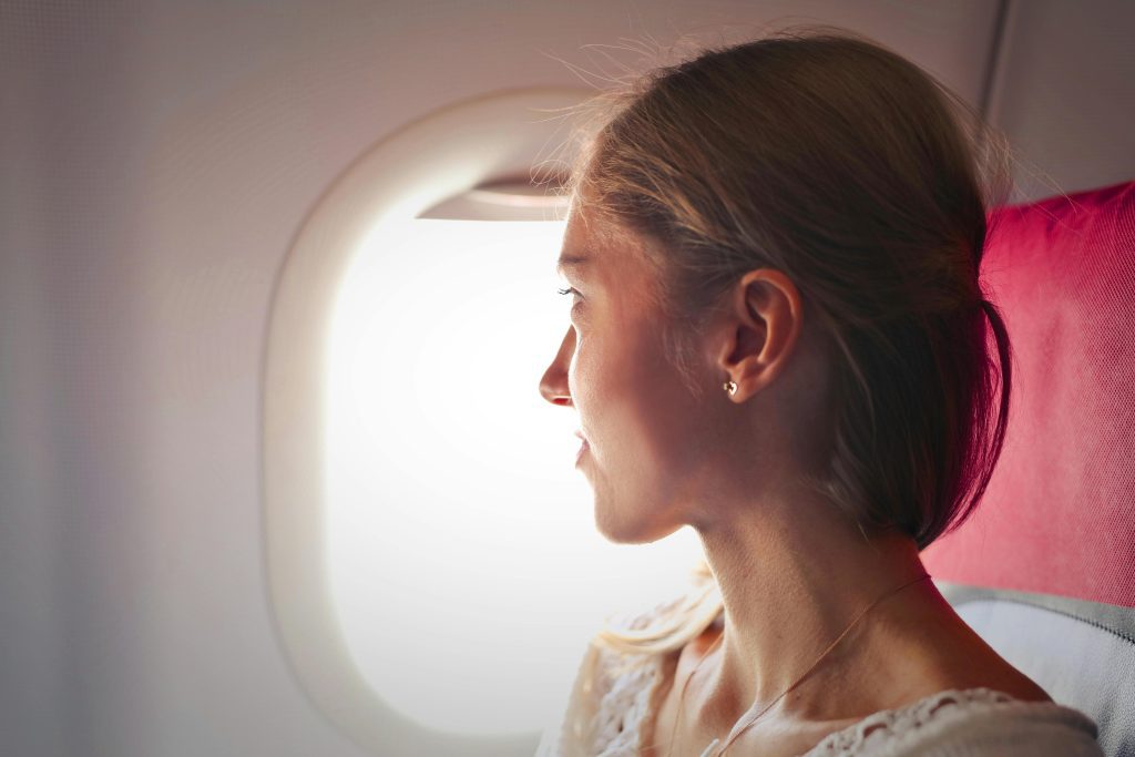 A woman gazes thoughtfully out the window of an airplane during her journey.