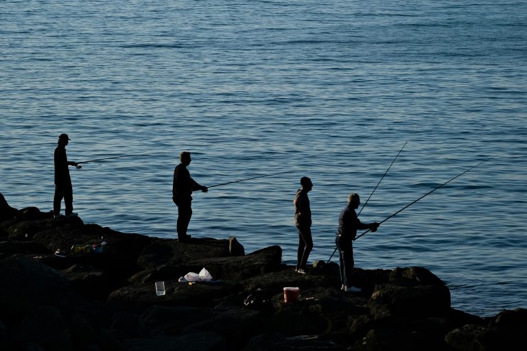 Silhouetted fishermen casting lines at dusk by the sea in Trabzon, Türkiye. Seen on Black Sea Cruises
