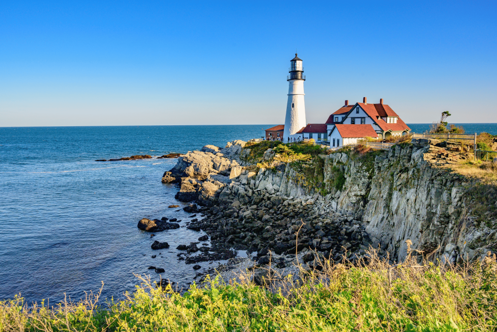 White lighthouse on the Maine coast surrounded by autumn foliage during New England in the fall holidays