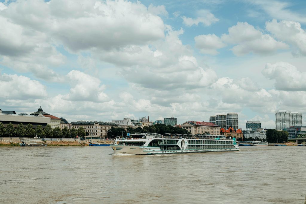 Scenic view of a cruise ship sailing the Danube River against the Bratislava skyline under a cloudy sky.
