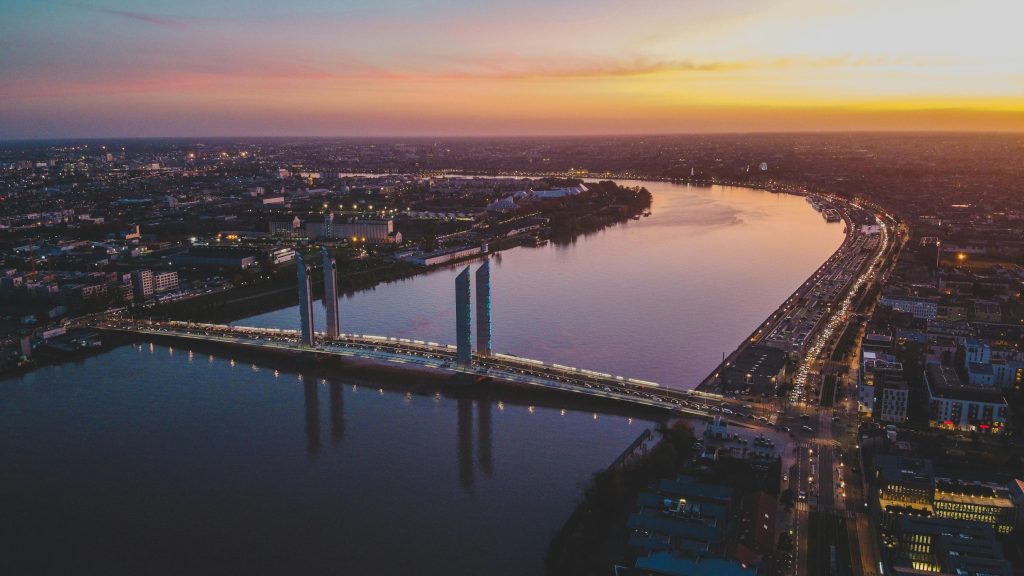 A stunning aerial view of Bordeaux's modern bridge and skyline at sunset over the Garonne River.