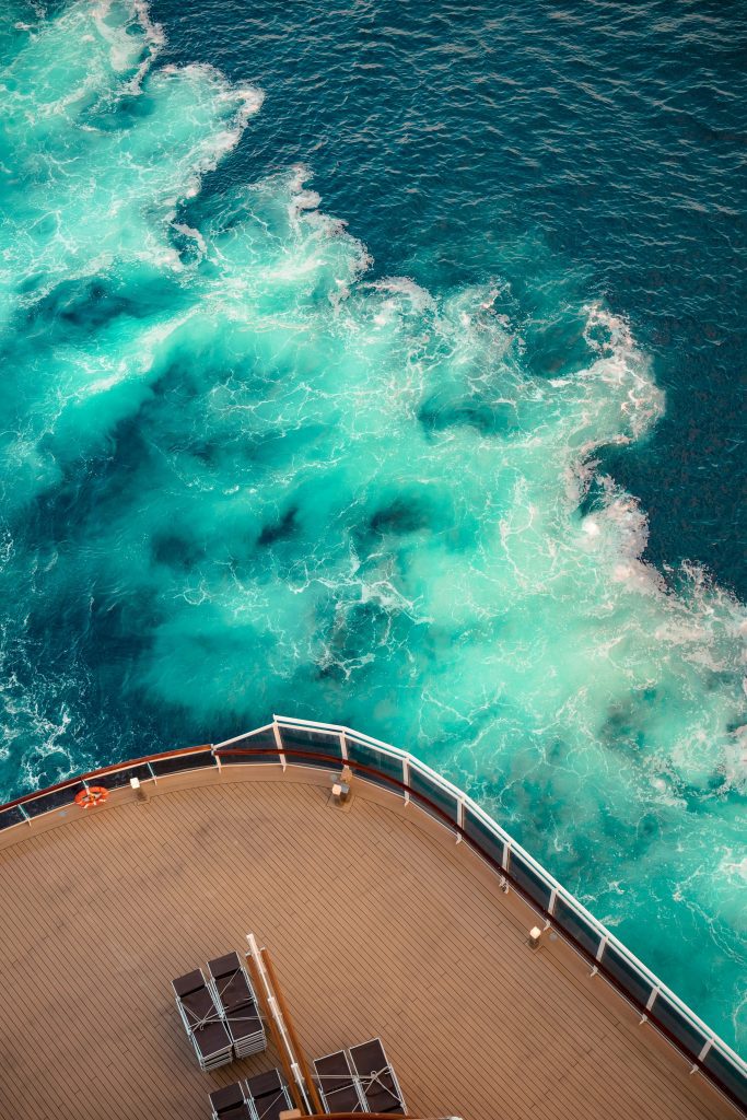 Top view of a cruise ship deck overlooking vibrant turquoise ocean waves.